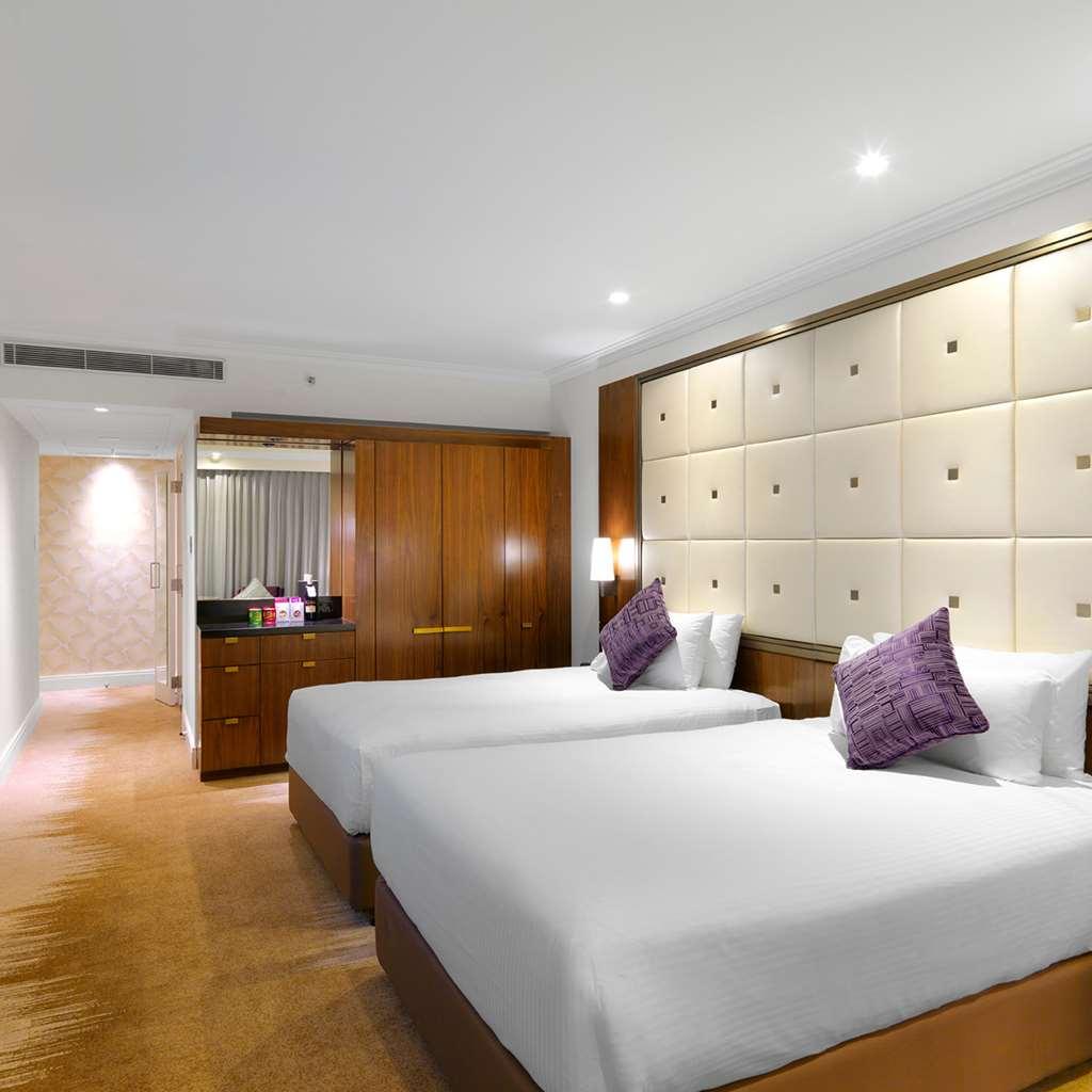 Amora Hotel Jamison Sydney Pokój zdjęcie The photo shows a modern hotel room featuring two twin beds with white bedding and purple decorative pillows. The walls are designed with soft beige panels, creating a luxurious ambiance. There’s wooden furniture, including a cabinet against one wall